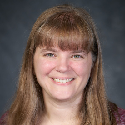 A person with long, light brown hair standing against a dark background.