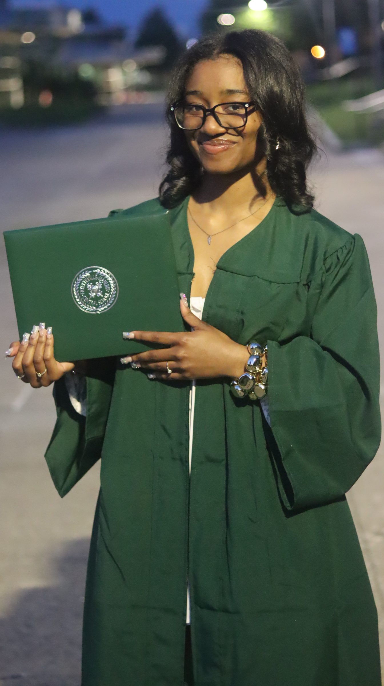 Young woman in a green graduation gown holding a diploma