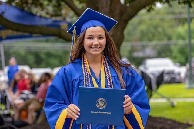 Young woman in a blue and yellow graduation cap and gown holding a blue diploma