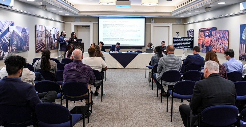 two people address others in a room during a panel discussion