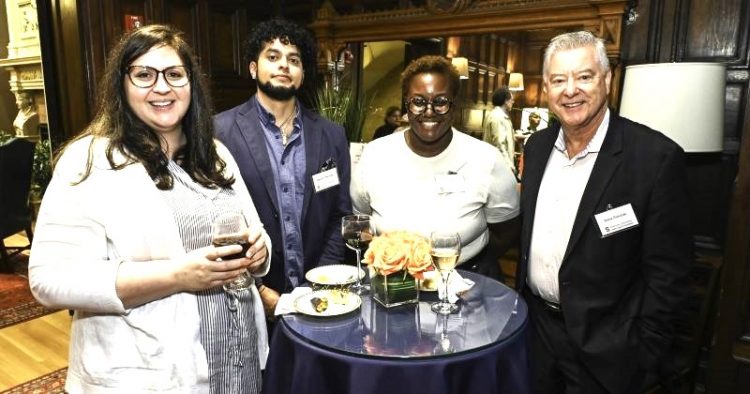 four people facing the camera attend a reception and face the camera smiling for a photo