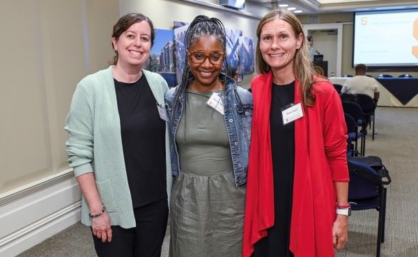 three people attending an event face the camera, smiling