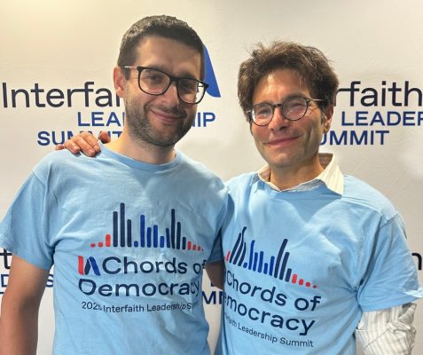 Imam Amir Duric and Rabin Natan Levy, both wearing glasses and smiling, both wearing light blue t-shirts that say Chords of Democracy