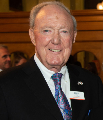 a person in formal attire, standing indoors with wooden paneling in the background