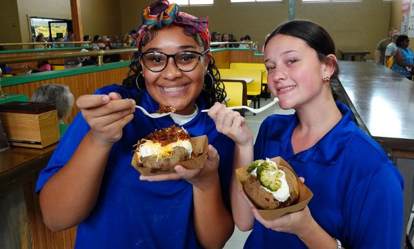 Two young women in blue shirts eating baked potatoes