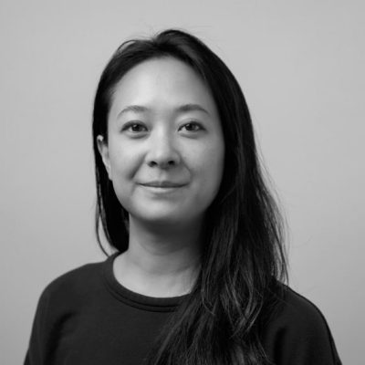 Black and white headshot of a woman with long dark hair wearing a dark sweater, smiling softly at the camera against a neutral background.
