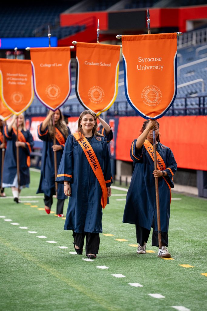 University and school and college marshals walk into the JMA Wireless Dome with orange banners