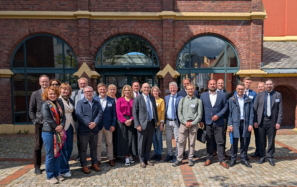 Group of 17 people in business attire standing outside a brick building labeled "DET JURIDISKE FAKULTET."