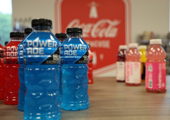 Powerade and Vitamin Water bottles with a Coca-Cola banner in the background