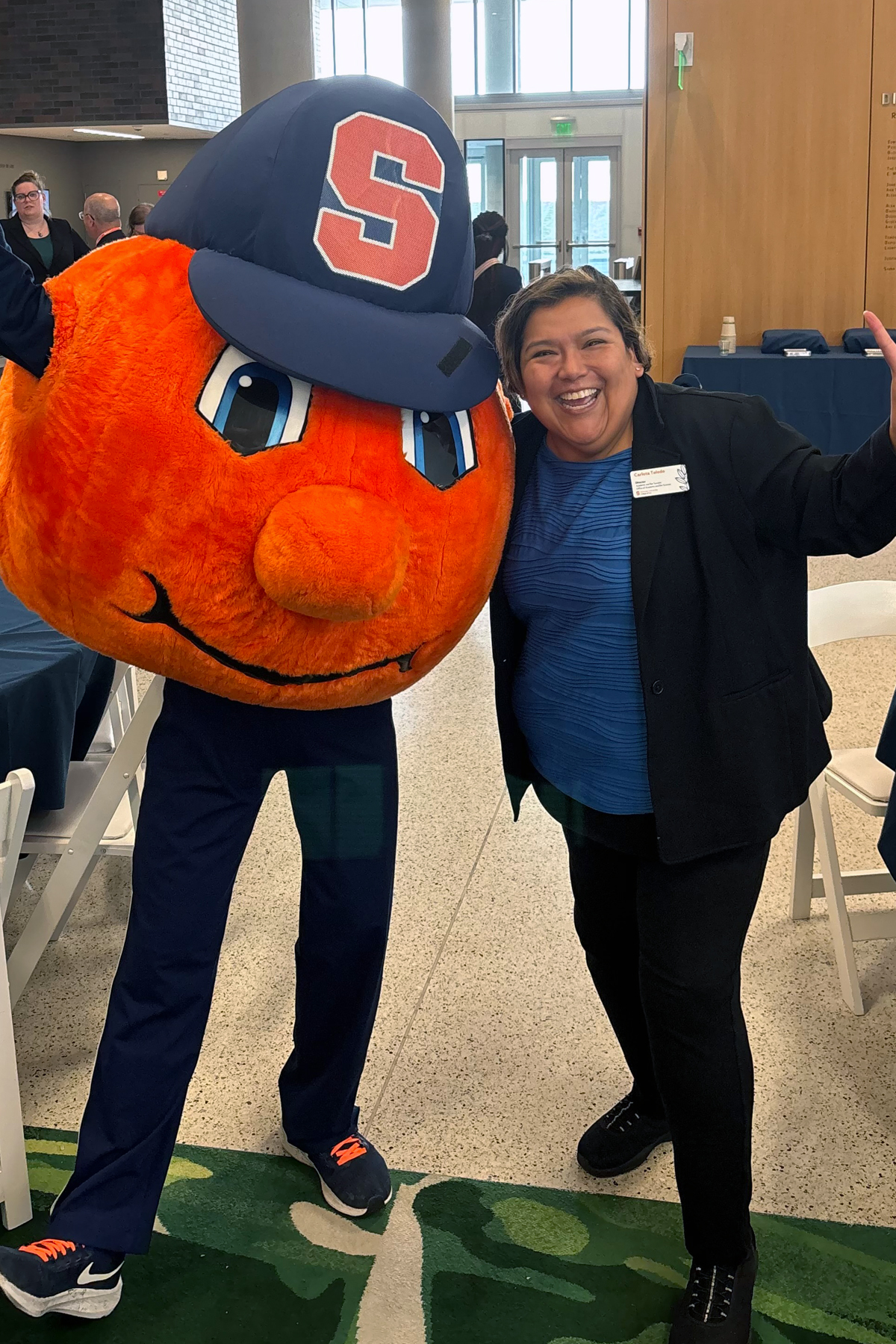 A person smiles while posing with Otto the Orange.