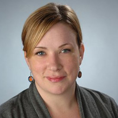 A person poses for a headshot in front of a gray backdrop.