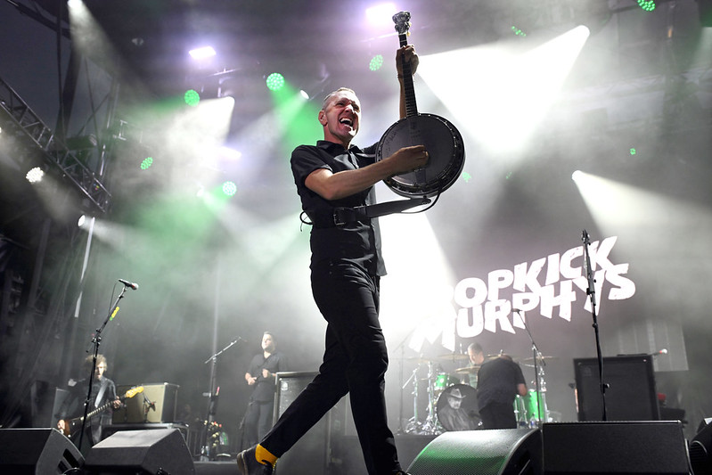 Performer on stage holding a guitar with white and green lights in the background