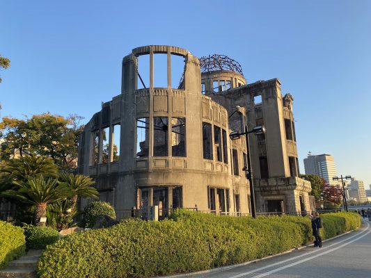 The Atomic Bomb Dome in Hiroshima, Japan, with its exposed steel dome and preserved walls, surrounded by greenery at sunset.