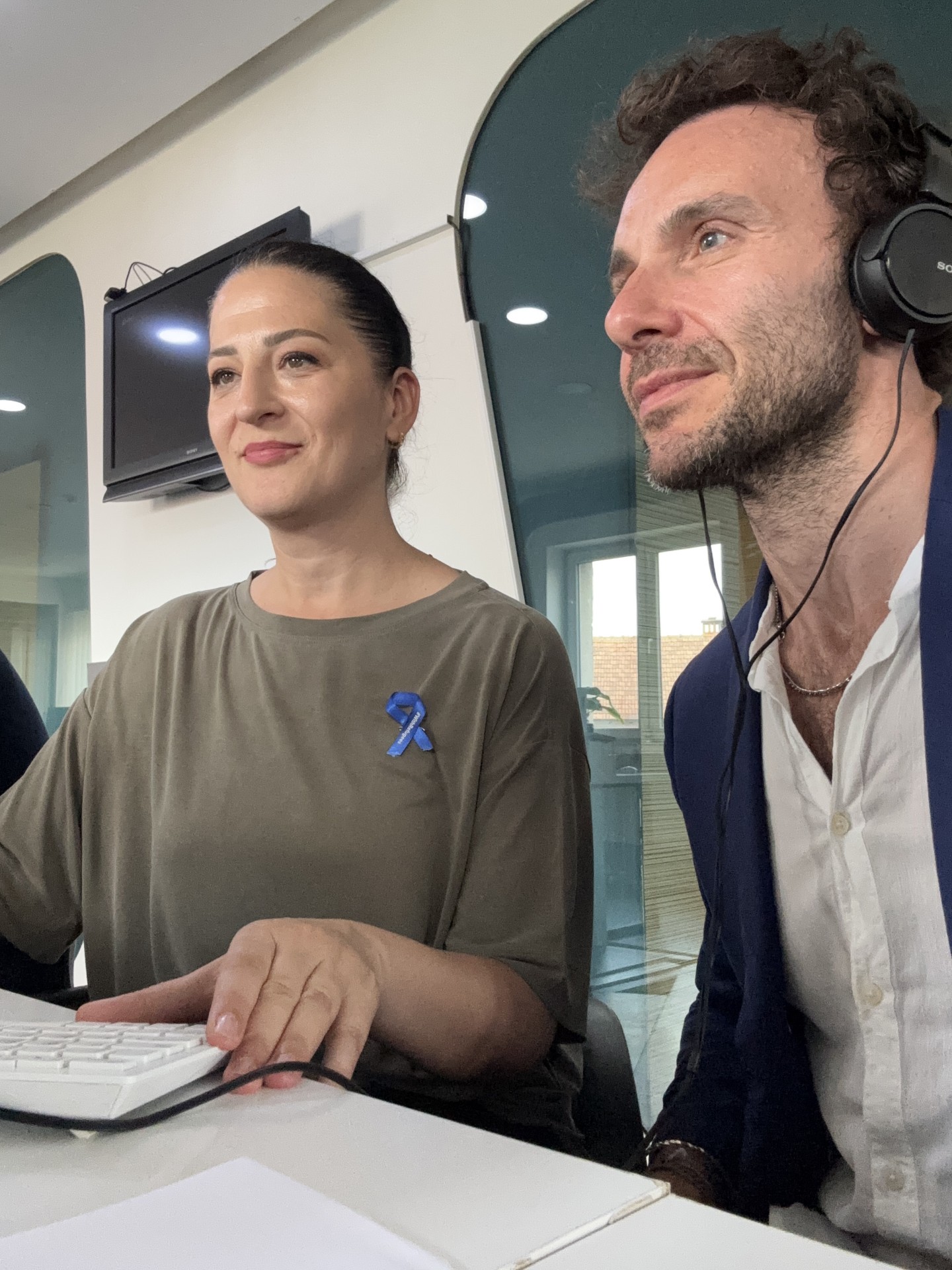 Two people, a man and a woman, are seated. Man is wearing headphones.