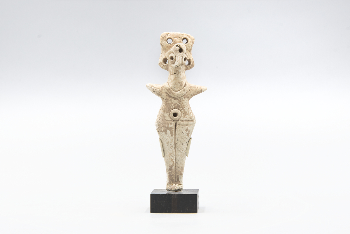 stone or clay figurine with stylized human features and multiple holes, displayed on a black rectangular base
