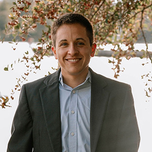 Man in blue shirt and grey jacket smiling