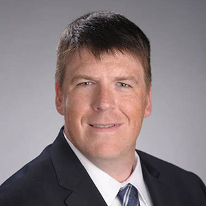 Man smiling, wearing a white shirt, blue jacket and tie