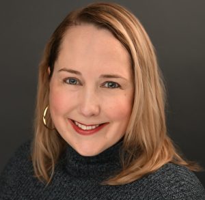 A professor smiles while posing for a headshot in front of a dark background.