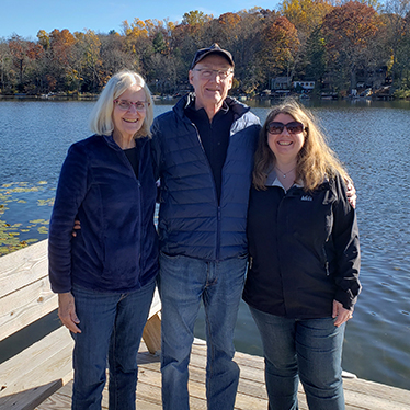 Two women and a man standing on a dock with fall foliage in the background