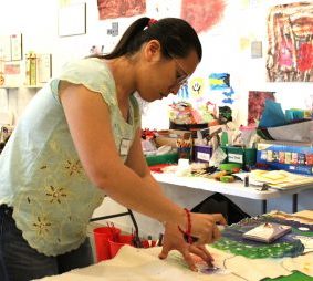 Doctoral economics student Brenda Teruya collects data for the “Corpórea” exhibition in a room with art supplies and colorful wall art.