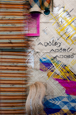 Woven textile artwork with striped fabric on the left and intricate patterns, colorful threads, and yarn bundle on the right.