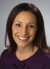 A woman smiles for a headshot in front of a grey backdrop.
