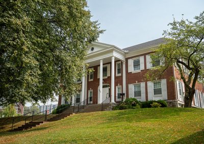 large, two-story brick building with white columns and trim, featuring a central entrance with steps leading up to it