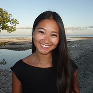 Woman, smiling, in black blouse with trees, water and sky in background
