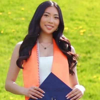A student smiles while holding their degree on the Syracuse University campus.