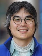 A person wearing a blue jacket and light green shirt with a white turtleneck underneath.