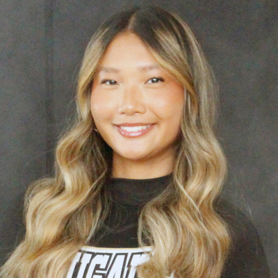 A student smiles while posing for a headshot in front of a grey backdrop.