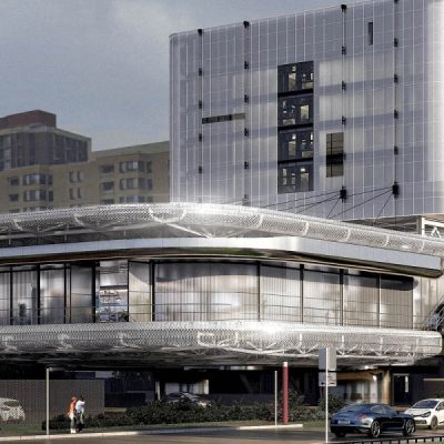 Circular modern building with mesh exterior and glass windows, with two people walking nearby.