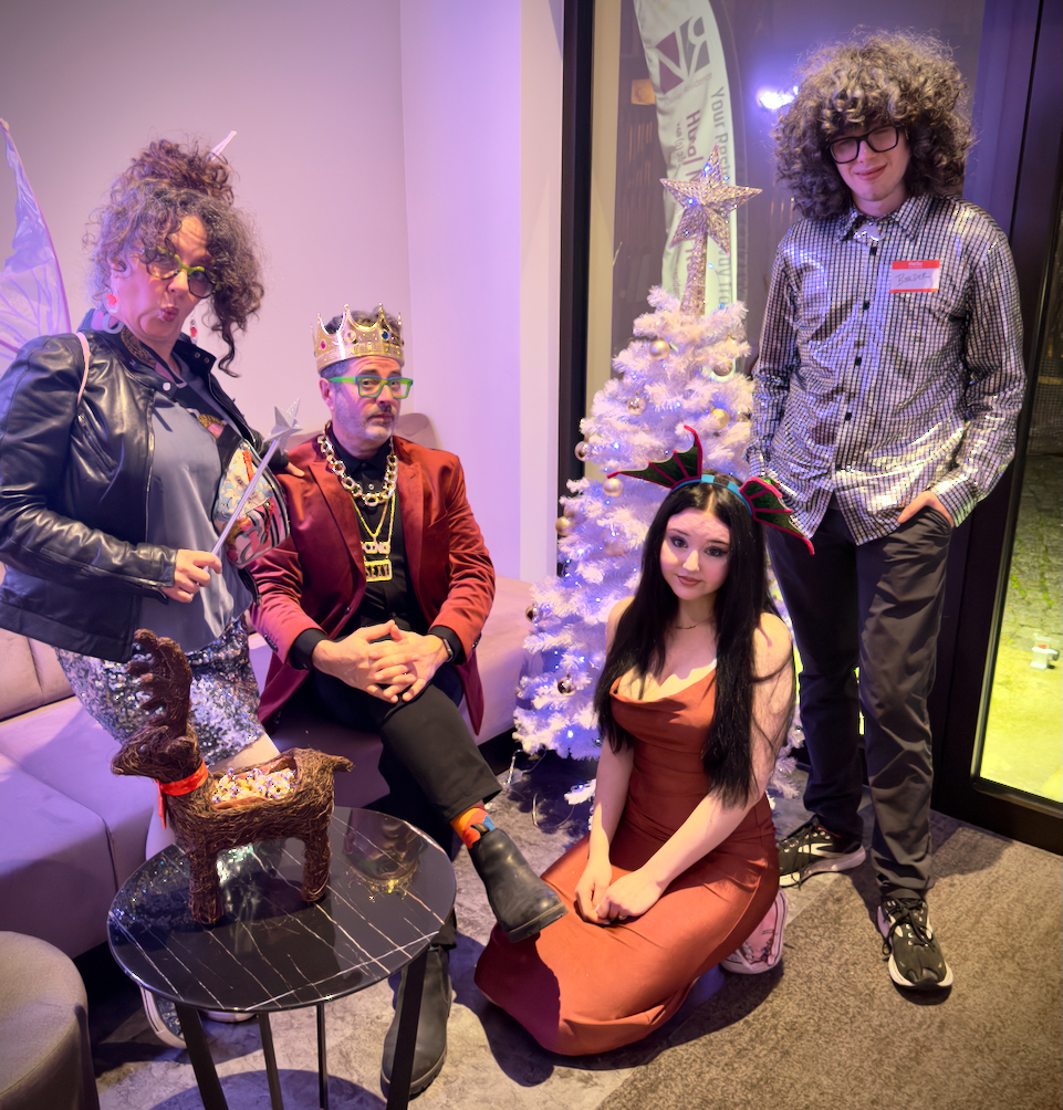 Four people in festive attire posing in front of a decorated white Christmas tree with ornaments and a star topper