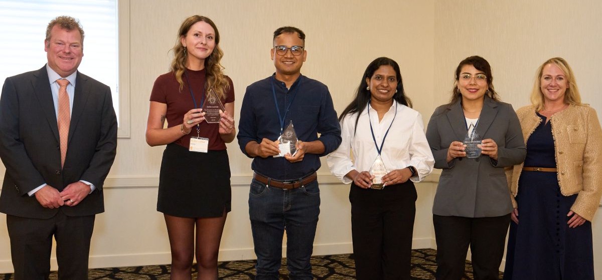 Six people standing in a room, the four in the center holding awards.