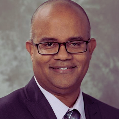 A person smiles while posing for a headshot in front of a grey backdrop.