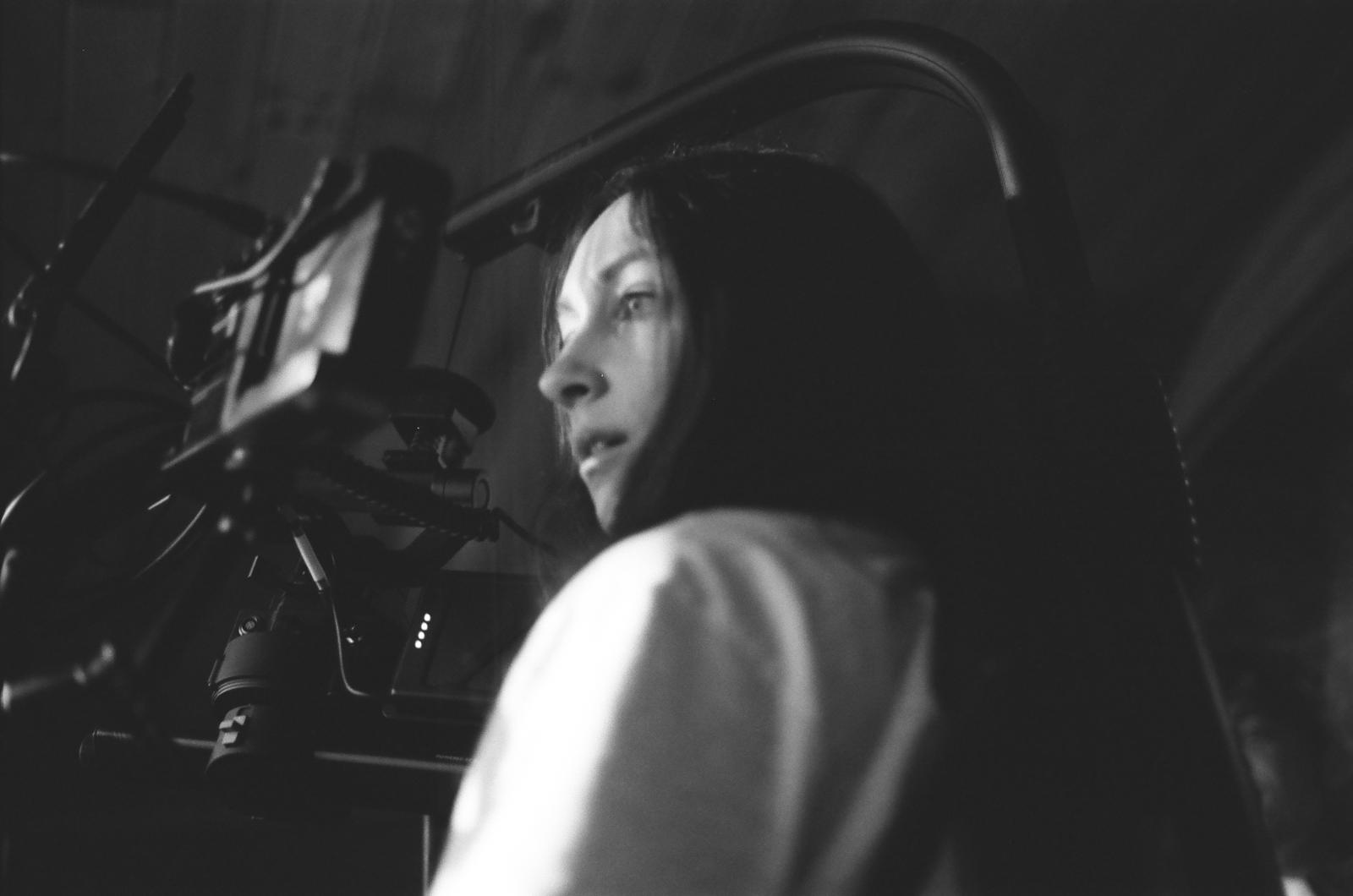 A person in profile looking through or operating a large film camera, with dramatic lighting creating shadows across their face