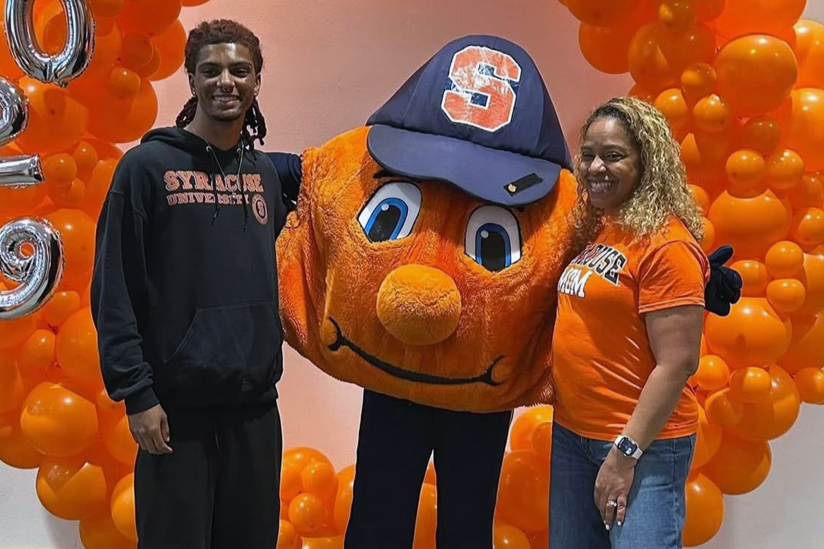Two students pose with Syracuse University's orange mascot Otto in front of an orange balloon display at a campus event.