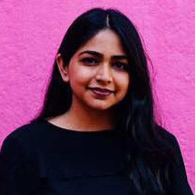 A person poses for a headshot in front of a pink backdrop while wearing a black shirt.