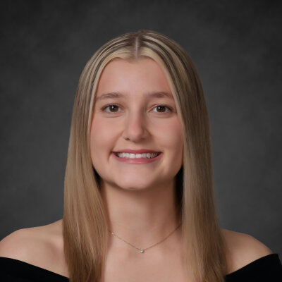 A student smiles while posing for a headshot in front of a grey backdrop.