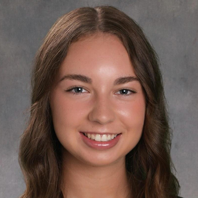 A student smiles while posing for a headshot in front of a grey backdrop.