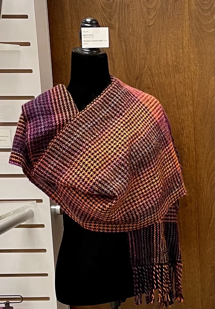 Woven shawl with a warm gradient houndstooth pattern and fringed ends, displayed on a mannequin