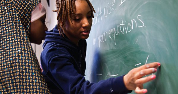 A Syracuse University student works with a Syracuse City School District student at a chalkboard as part of the Literacy Corps program