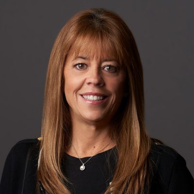 A person smiles while posing for a headshot in front of a grey backdrop.