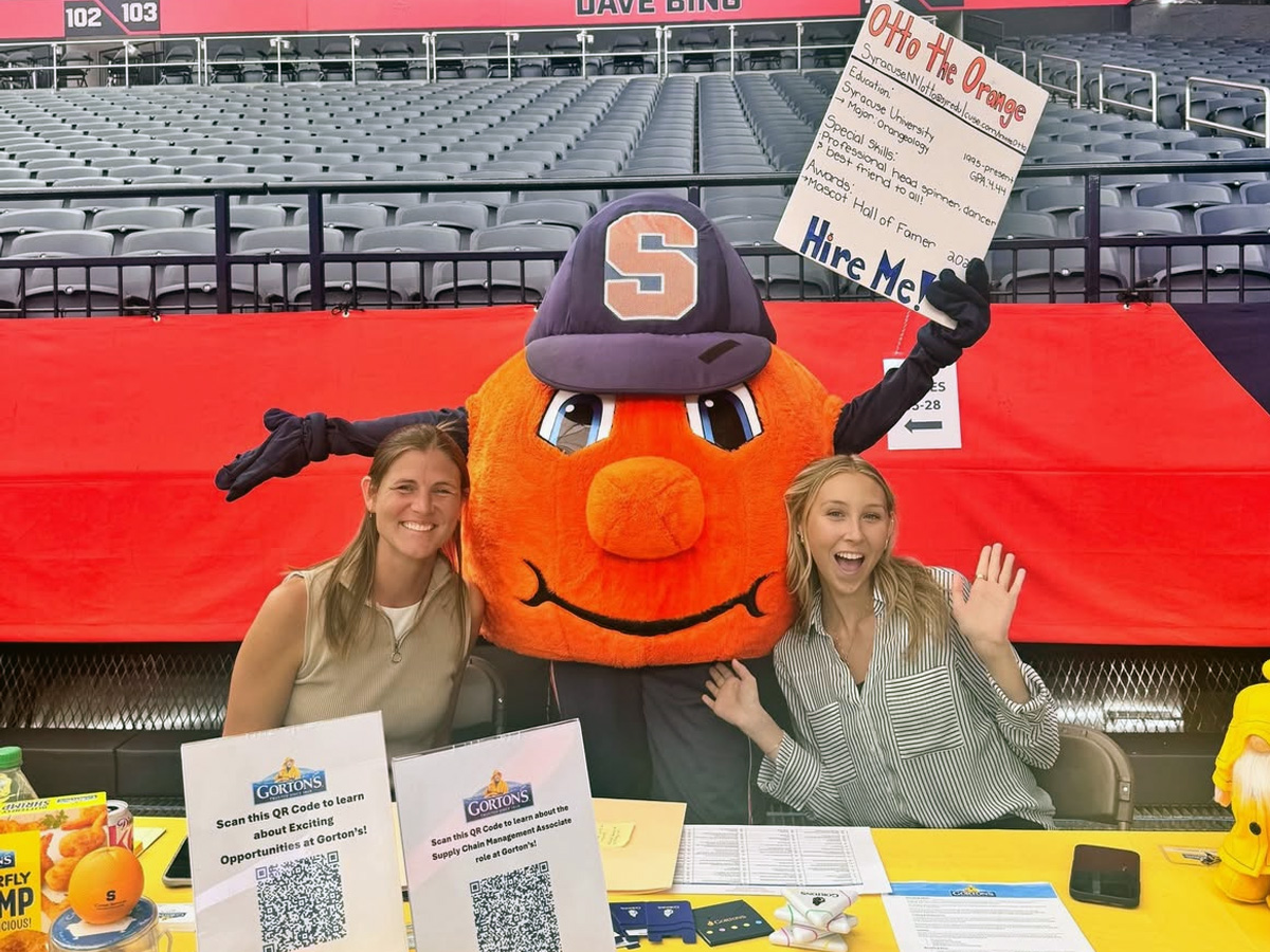 Otto the Orange mascot posing with two individuals at a career fair table promoting Gorton's job opportunities
