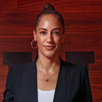 A person wearing a red Chicago satin jacket and white top, holding a basketball, smiling in front of wooden shelving.