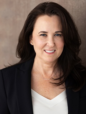 Person wearing a black blazer over a white shirt, standing against a neutral textured background.