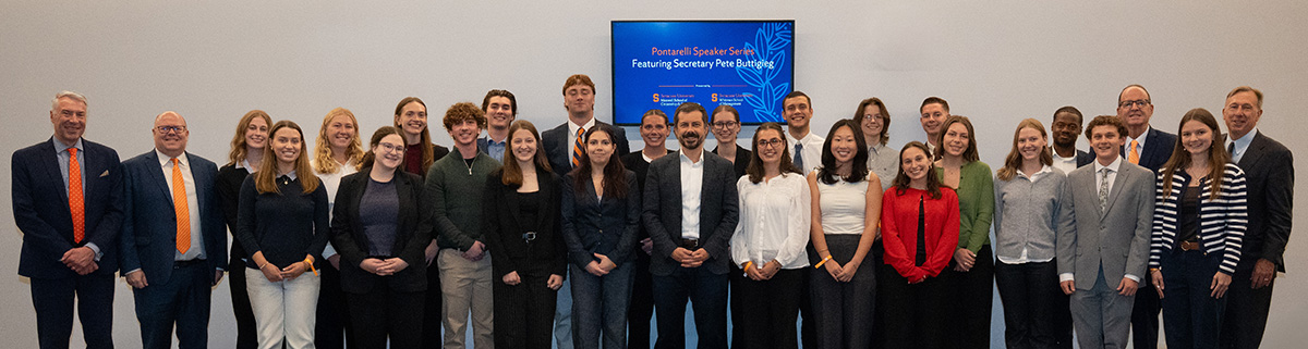 Group of people posing for a photo at the Maxwell School, standing in front of a sign that reads "Pontarelli Speaker Series Featuring Secretary Pete Buttigieg" and Maxwell and Whitman School logos