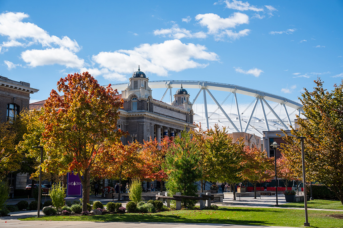 View of Syracuse University campus in autumn, featuring colorful fall trees and buildings under a blue sky with clouds.