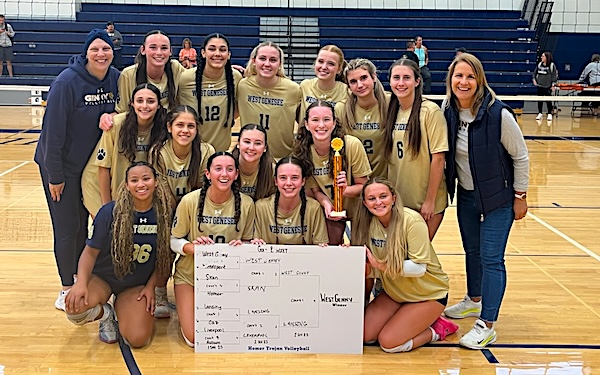 West Genesee volleyball team poses in gym with trophy and match results board.