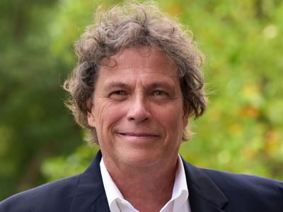 A professor smiles while posing for a headshot outside.